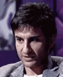 a close up of a man 's face with a purple background behind him .