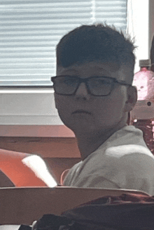 a boy wearing glasses and a white shirt looks at the camera