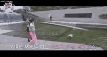 a woman in pink pants is walking in front of a waterfall and a sign that says honeycam.org