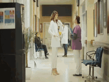 a woman in a lab coat talking to a nurse in a hospital hallway