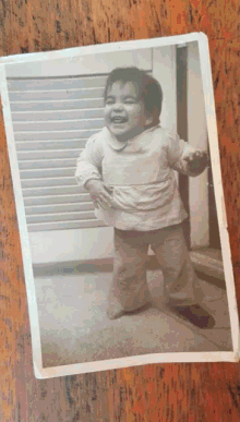 a black and white photo of a little girl laughing on a wooden table