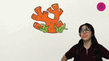 a woman wearing glasses stands in front of a drawing of a coral and the number 4