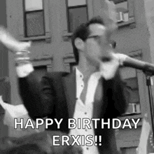 a man in a suit and tie is singing into a microphone and says `` happy birthday erxis '' .