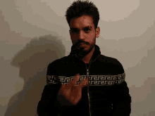 a man with a beard wearing a black jacket with a greek key pattern