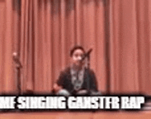a man is singing into a microphone in front of a red curtain with the words `` me singing gangster rap '' .