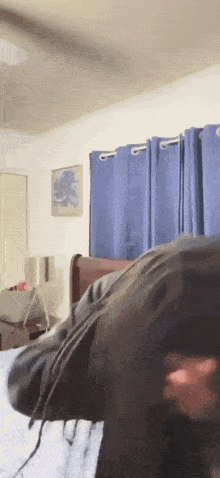 a person laying on a bed in a room with blue curtains