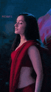 a woman in a red saree is standing in front of a purple flower .