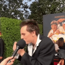 a man in a suit is talking into a microphone in front of a sign that says netflix