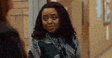 a woman with curly hair is standing in a hallway looking at another woman .