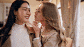 two women are standing next to each other and one is kissing the other 's cheek .