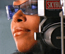 a close up of a woman wearing headphones and sunglasses with a sign that says ' skyro ' on it