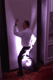 a man in a white shirt and black pants is dancing in front of a purple light