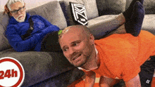 a man in an orange shirt is doing push ups next to a man laying on a couch