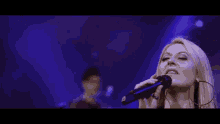 a woman singing into a microphone with a man behind her