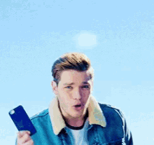 a man wearing a blue denim jacket with a white collar is standing in front of a blue sky .