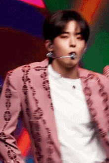 a man wearing a pink jacket and a white shirt is singing into a microphone