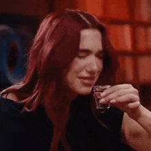 a woman with red hair is holding a shot glass in her hand and drinking from it .