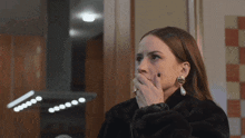 a woman covering her mouth with her hand while wearing earrings and a fur coat
