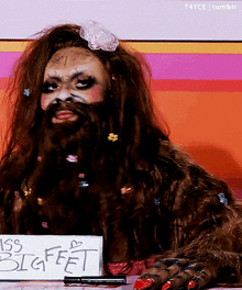 a woman with a beard is holding a sign that says miss big feet