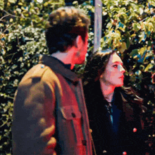a man and a woman are standing next to each other in front of trees