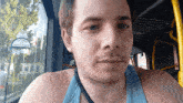 a man wearing a blue tank top is looking at the camera with a sign in the background that says autobus haltesstelle