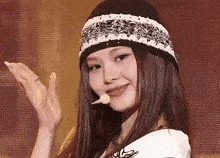 a woman wearing a hat and a headband is smiling and waving .