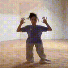 a woman in a blue shirt and grey pants is dancing in a room