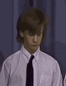 a young man in a white shirt and black tie is looking down .