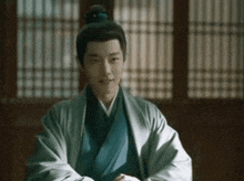a man in a kimono is sitting in front of a window with his hands folded .