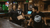 three men are standing in a bar with a beer sign above them