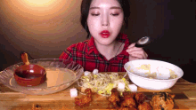 a woman in a plaid shirt is eating noodles and chicken