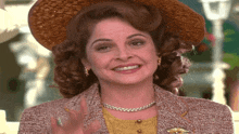 a woman wearing a hat and a jacket is smiling and waving