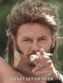 a man with a mullet and a beard is smoking a cigarette and pointing at the camera .