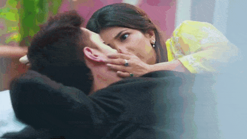 a woman in a yellow dress is kissing a man on the cheek .