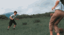 a boy and a woman are playing in a grassy field with the letter o on the bottom right