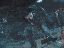 a man in a denim jacket stands in a dark room looking up