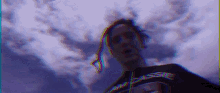 a man with dreadlocks is standing in front of a purple cloudy sky .