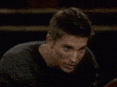 a man and a woman are talking to each other in a dark room . the woman is covering her mouth with her hand .