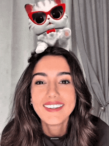 a woman with a stuffed cat on her head with sunglasses on