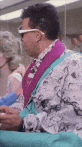 a man wearing sunglasses and a purple shirt sits in a chair