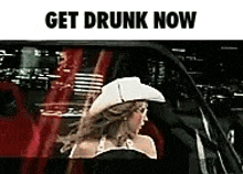 a woman in a cowboy hat is sitting in a car with the words `` get drunk now '' written above her .