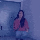 a woman in a red shirt and jeans is squatting in front of a blue door