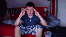 a young man sitting on a bed with his hands on his forehead