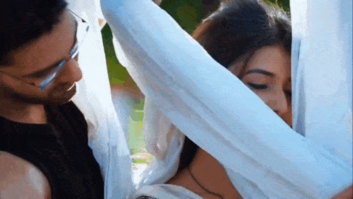 a man and a woman are standing next to each other and the woman is covering her face with a white cloth .