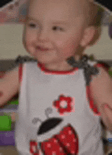 a baby is wearing a white tank top with a ladybug and a flower on it .