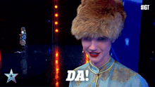 a man wearing a fur hat and a blue shirt says " da "