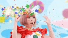 a woman in a clown costume is blowing confetti out of her mouth .