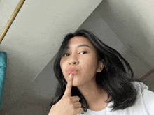 a woman holds her finger to her lips while wearing earrings