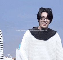 a man wearing glasses and a scarf around his neck is smiling for the camera ..