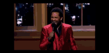 a man in a red suit is standing in front of a microphone and giving a speech .